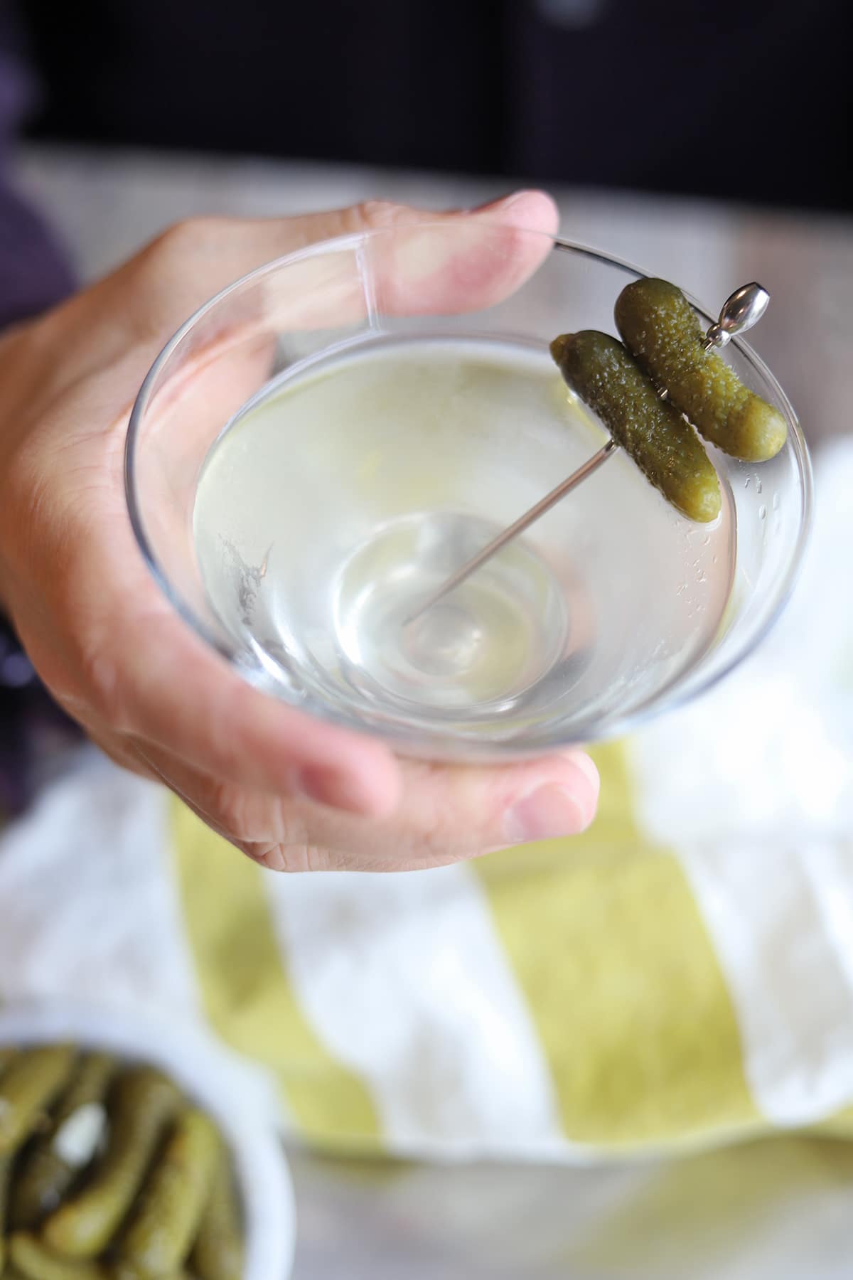 Hand holding pickle martini over table.