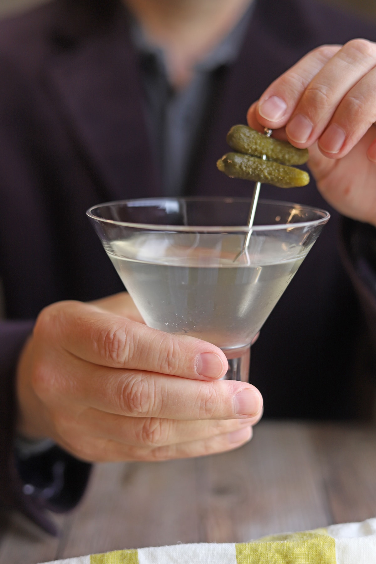 Hand lifting cornichon garnish from martini glass.