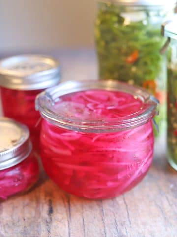 Glass jars of red pickled onions and jalapenos.