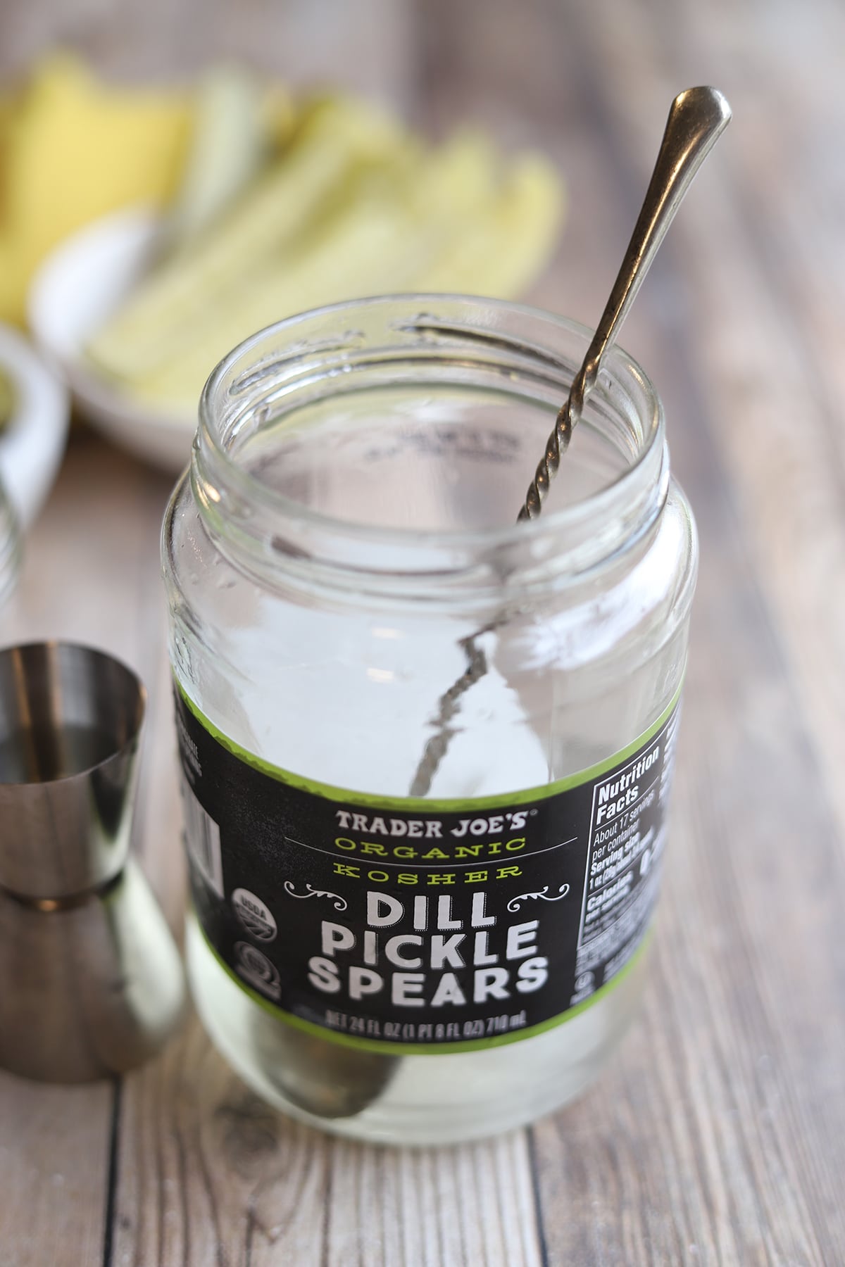 Empty pickle jar with ice, large spoon, and jigger for cocktail making.
