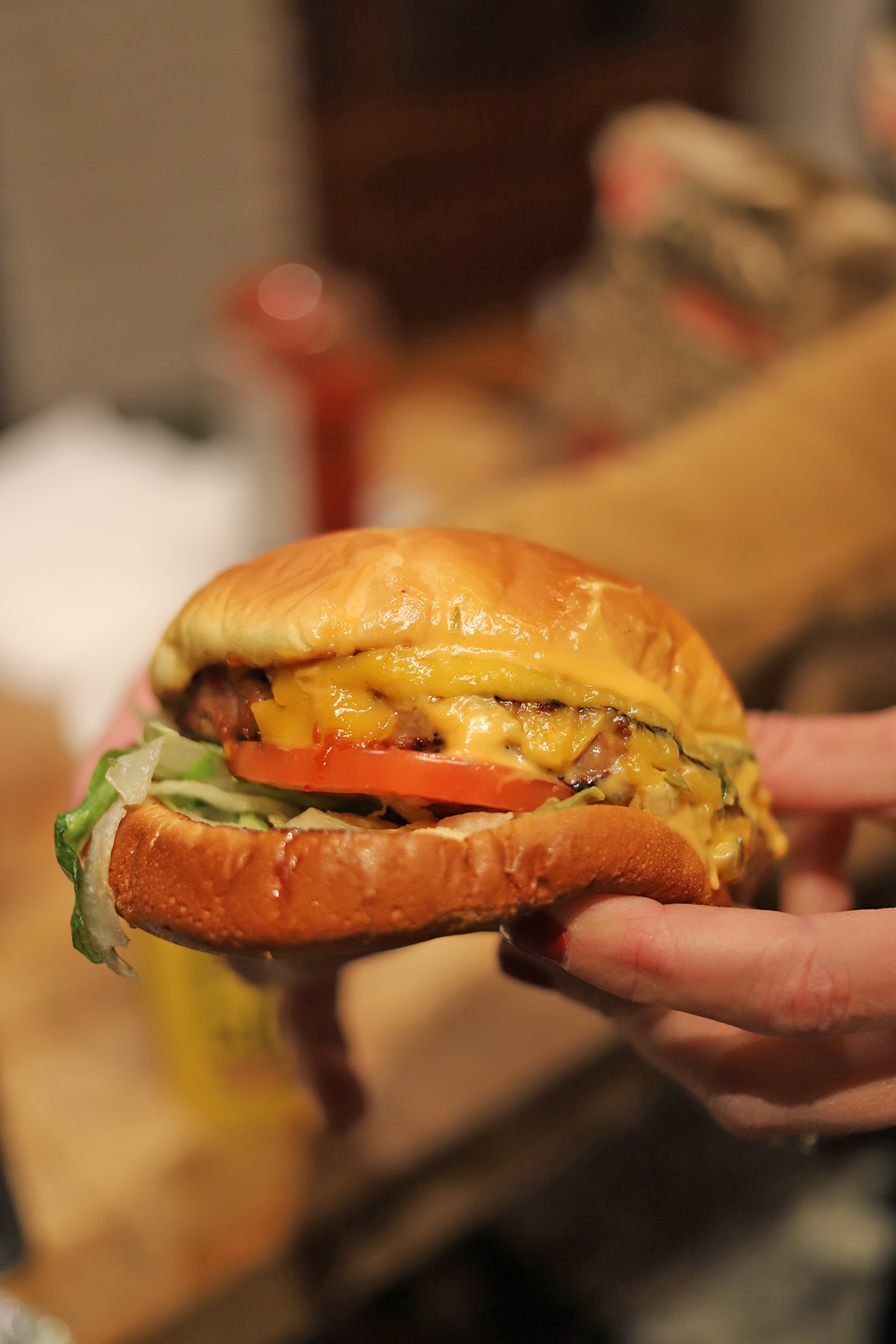 Hands holding burger with tomato slice.