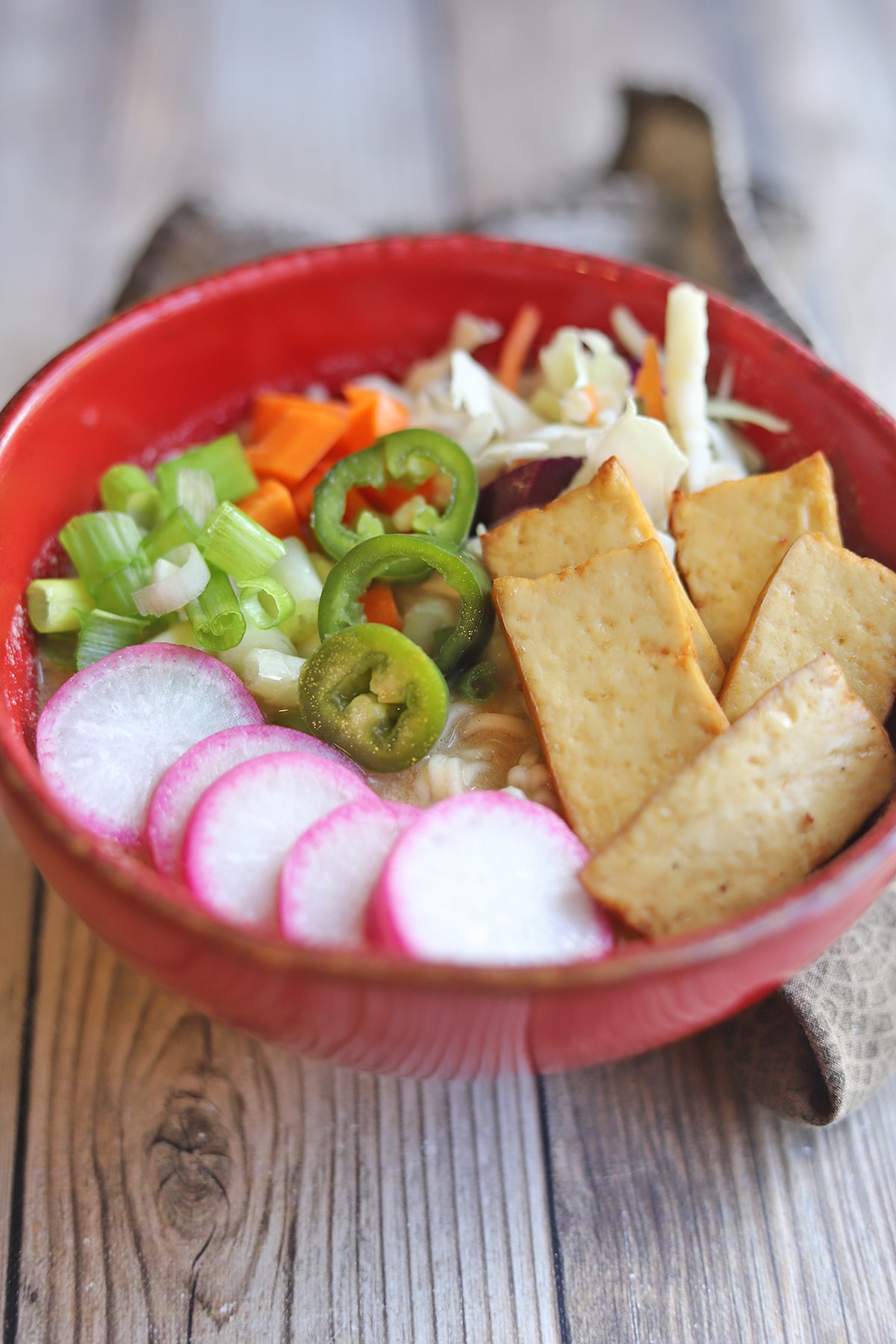 Bowl of ramen with tofu, jalapenos, radishes, onions, carrots, and cabbage.