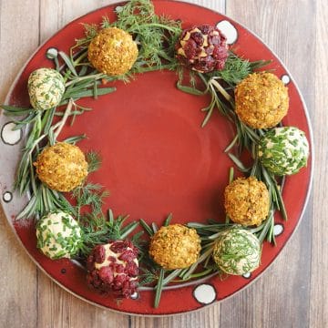 Red platter lined with rosemary, dill, and vegan cheese balls to make a wreath.
