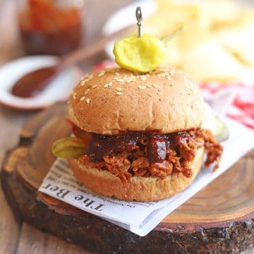 Barbecue jackfruit sandwich on table with barbecue sauce and potato chips.
