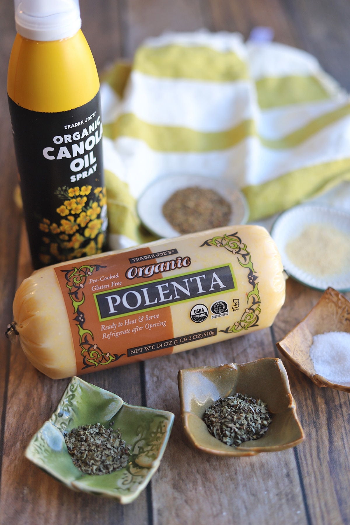 Chub of prepared polenta with oil spray, and spices on table.
