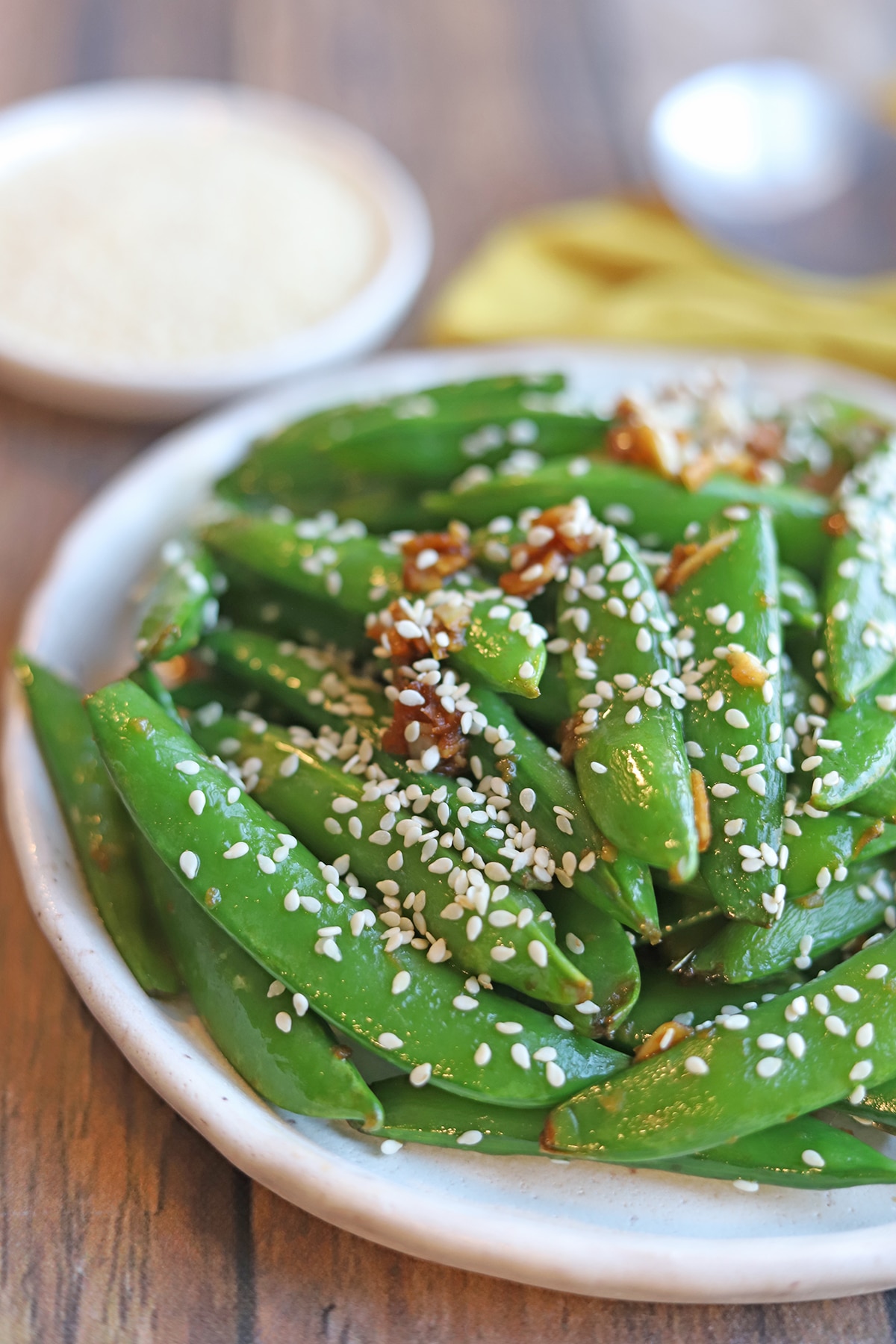 Close-up sugar snap peas on plate, garnished with sesame seeds.