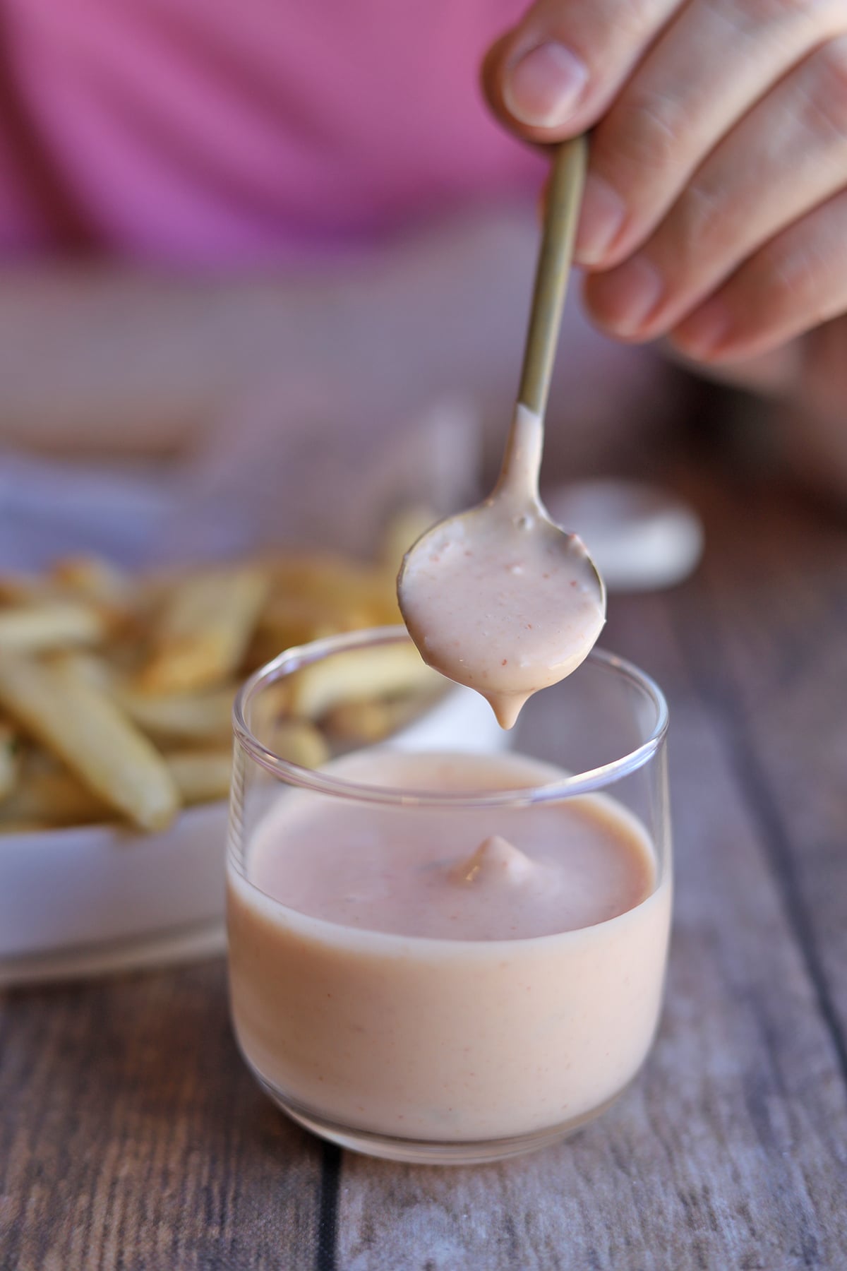 Sriracha mayo dipping off of spoon into glass.