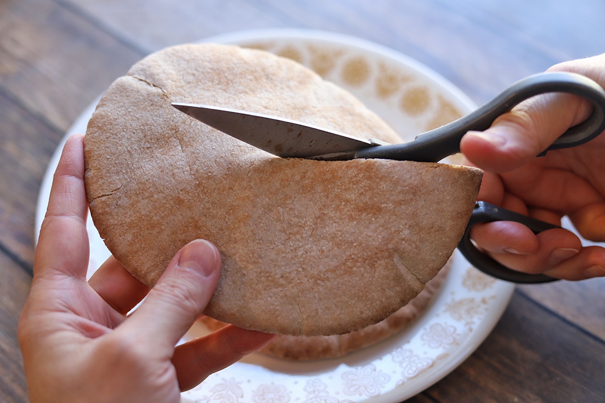 Hand cutting pita bread in half with scissors.