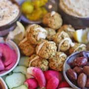Mezze style falafel platter with olives, hummus, and baba ganoush on tray.