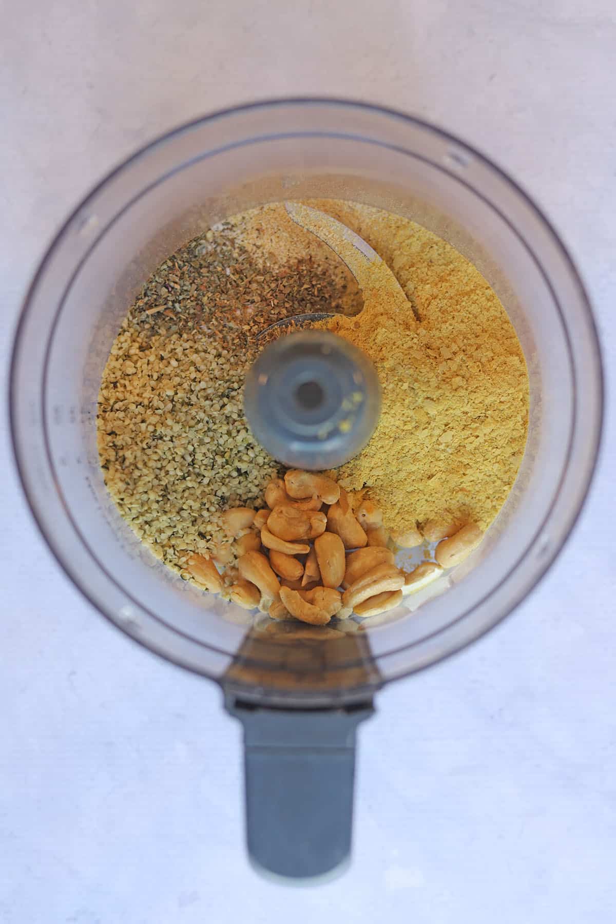 Cashews, hemp hearts, nutritional yeast, and spices in food processor bowl.