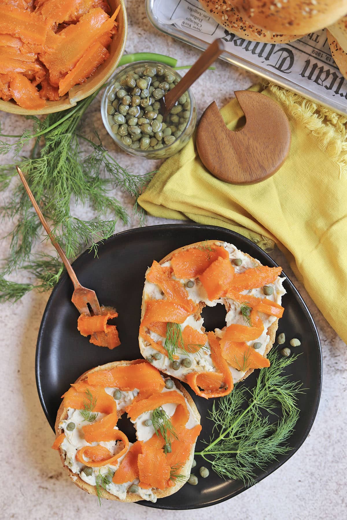 Bagels with vegan cream cheese and carrot lox on plate by yellow napkin.