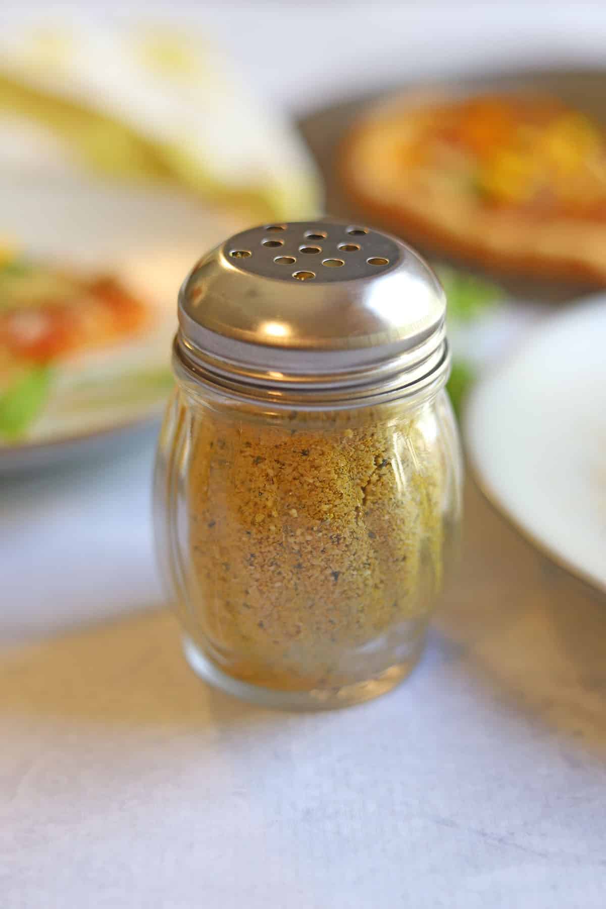 Cashew parmesan in shaker jar on table.