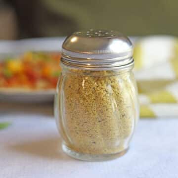 Jar of cashew parmesan on table by striped napkin.