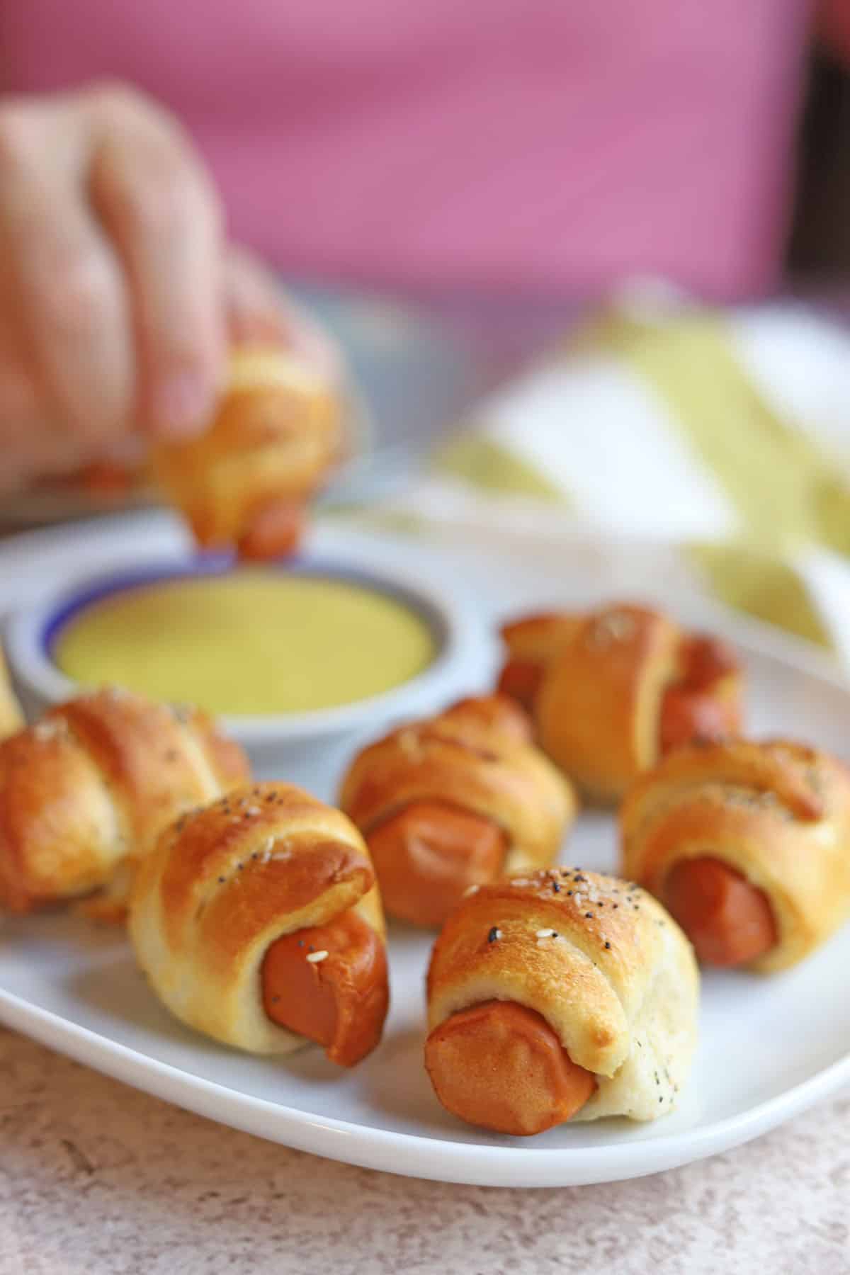 Platter of vegan pigs in a blanket with dipping sauce in background.