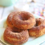 Text overlay: Baked vegan cinnamon donuts. Pile of doughnuts on a plate.