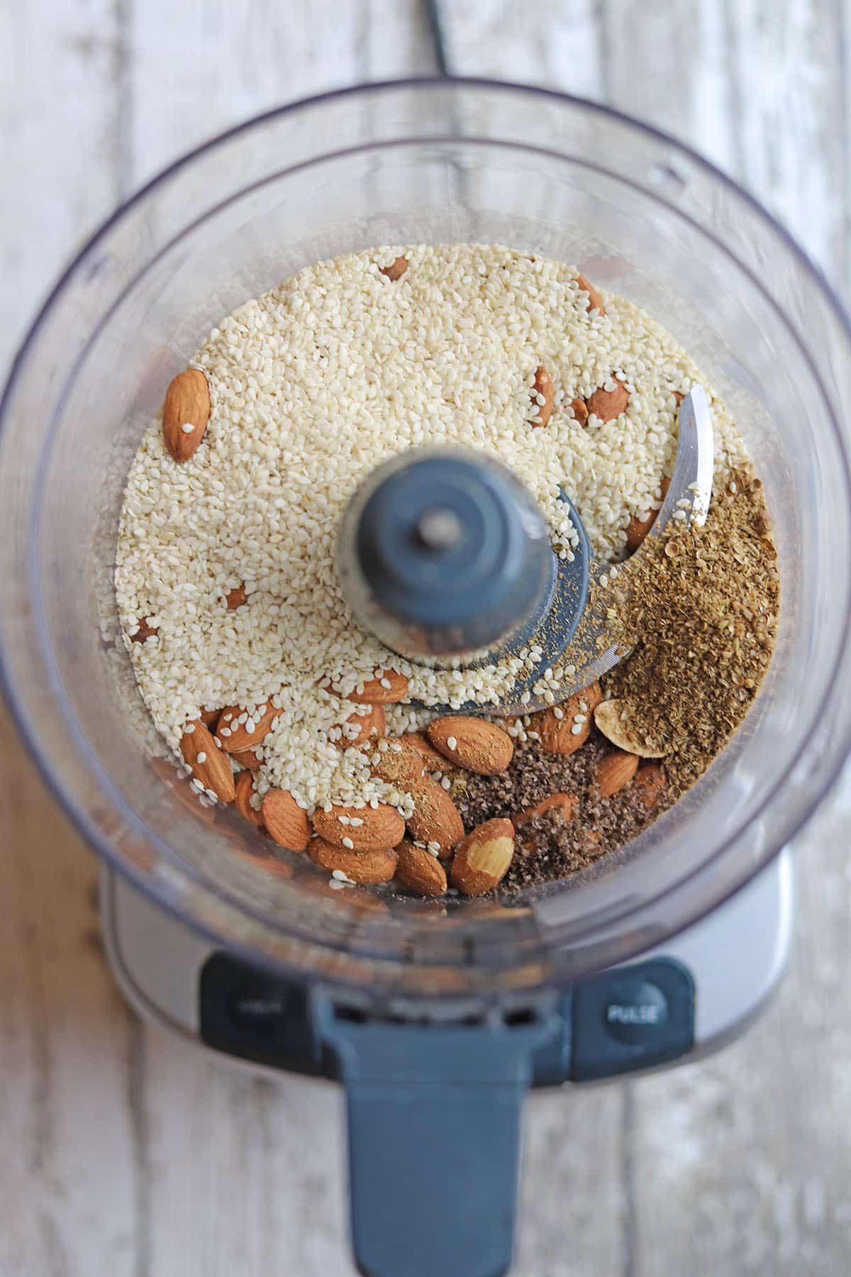 Almonds, spices, and sesame seeds in food processor bowl.