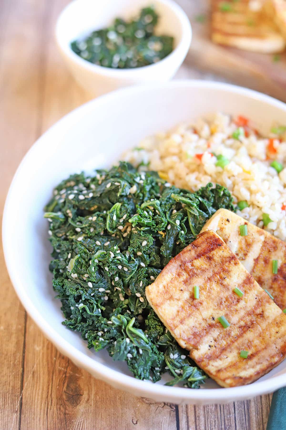 Steamed kale with sesame seeds in bowl with tofu and rice.