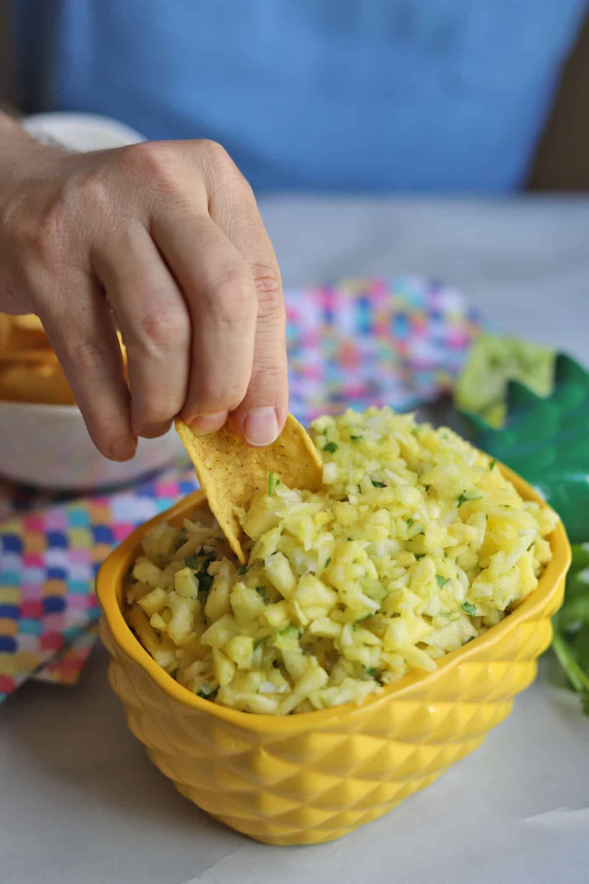 Tortilla chip being dipped into pineapple salsa.