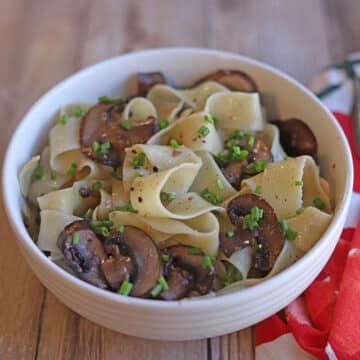 Bowl of pappardelle with red wine mushrooms by floral napkin.