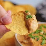Text overlay: The BEST vegan chili cheese dip. Tortilla chip with cheese sauce on top.