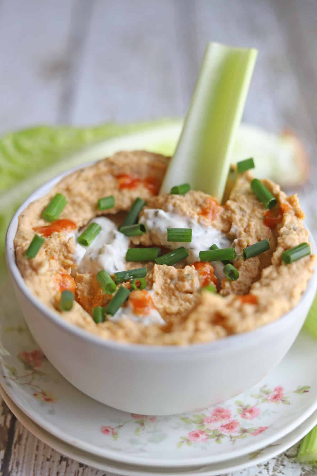 Buffalo hummus topped with vegan blue cheese in bowl with celery.