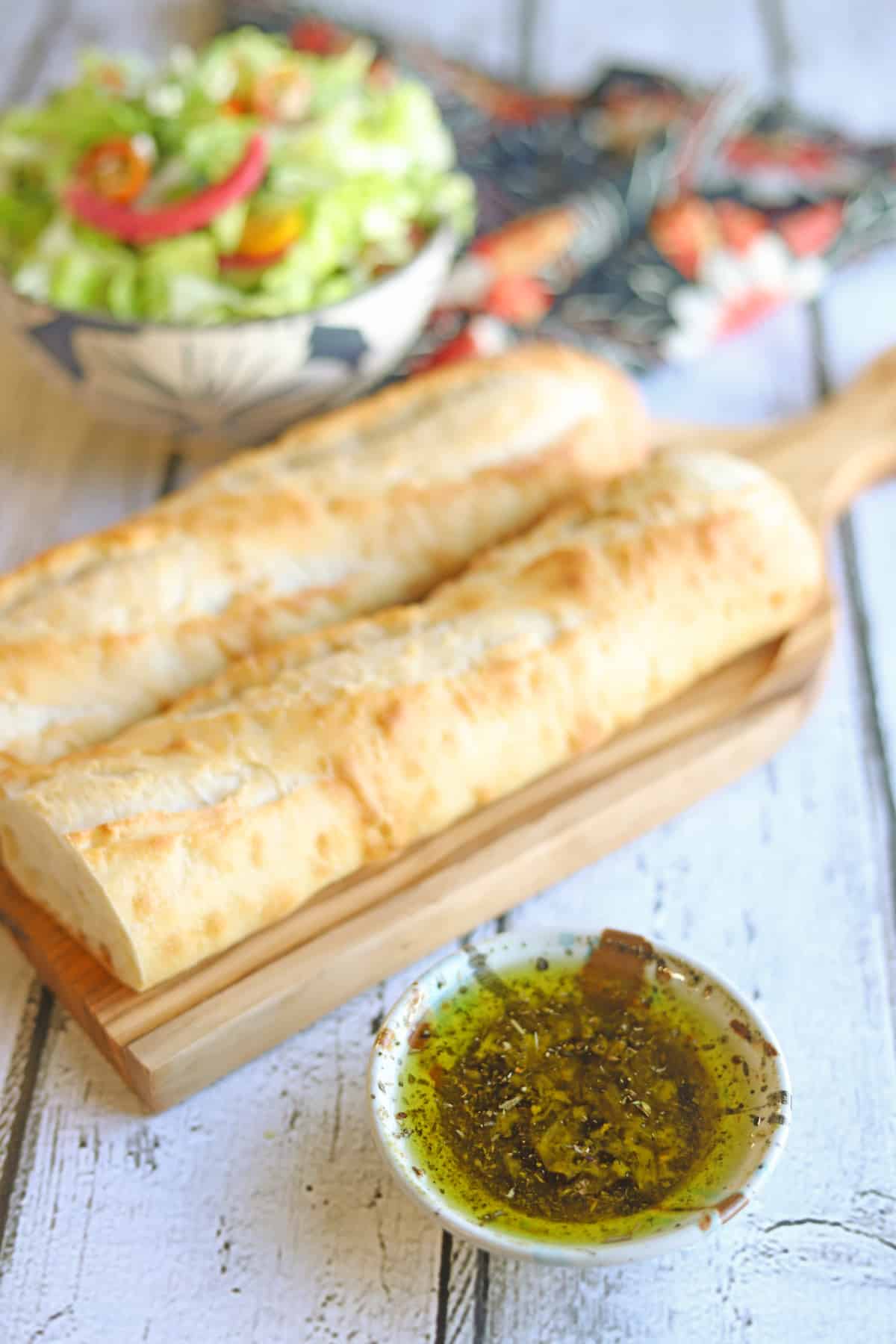 Seasoned olive oil with vinegar on table by baguette and salad.