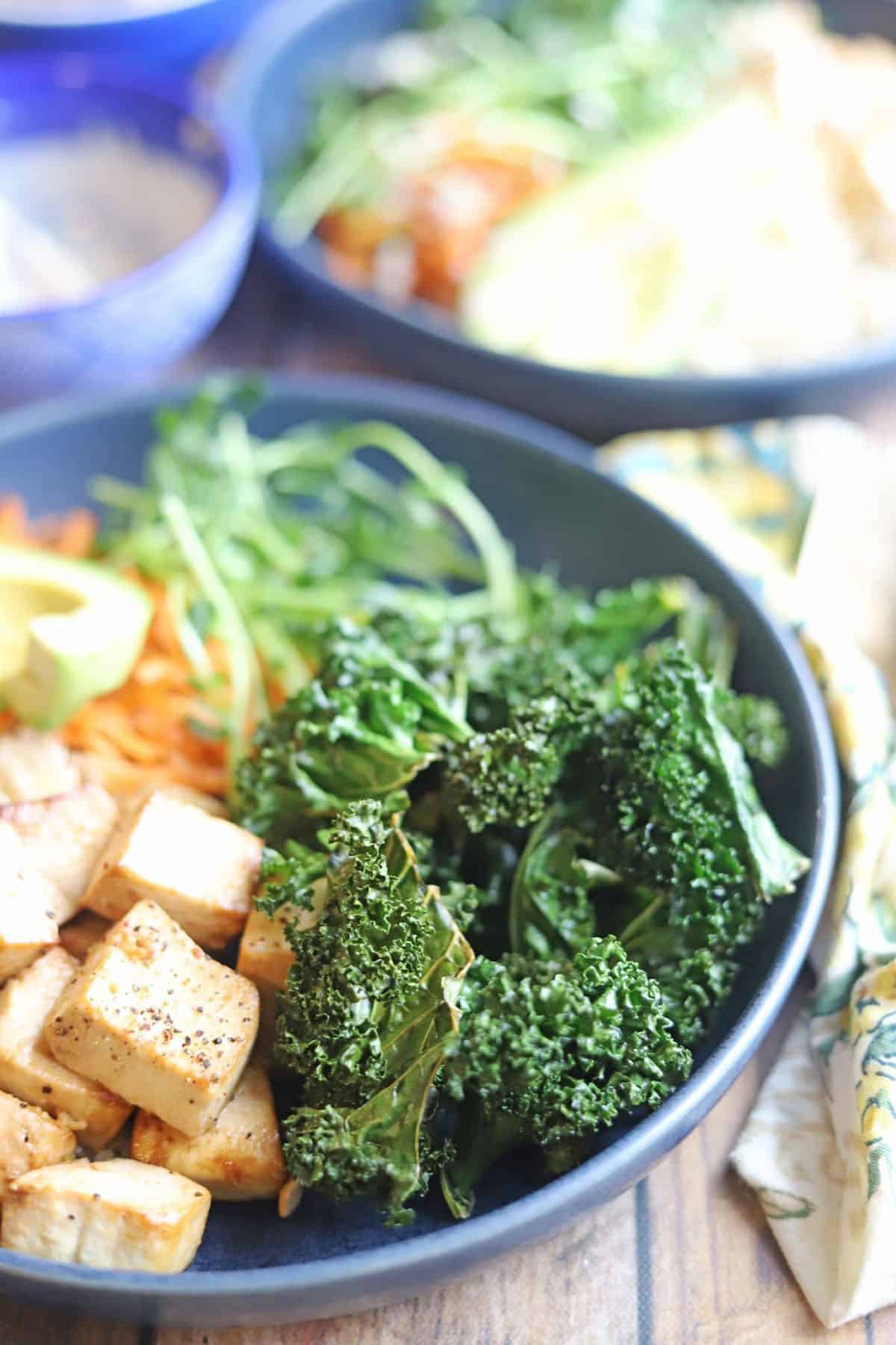 Crispy kale chips in bowl with tofu and sprouts.