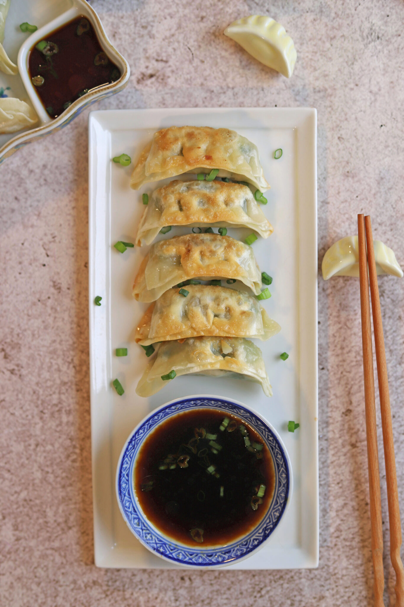 Gyoza on platter with dipping sauce by chopsticks.