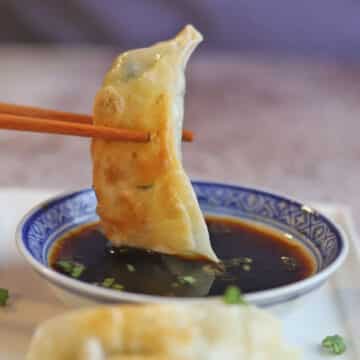 Gyoza being dipped into sauce with chopsticks.