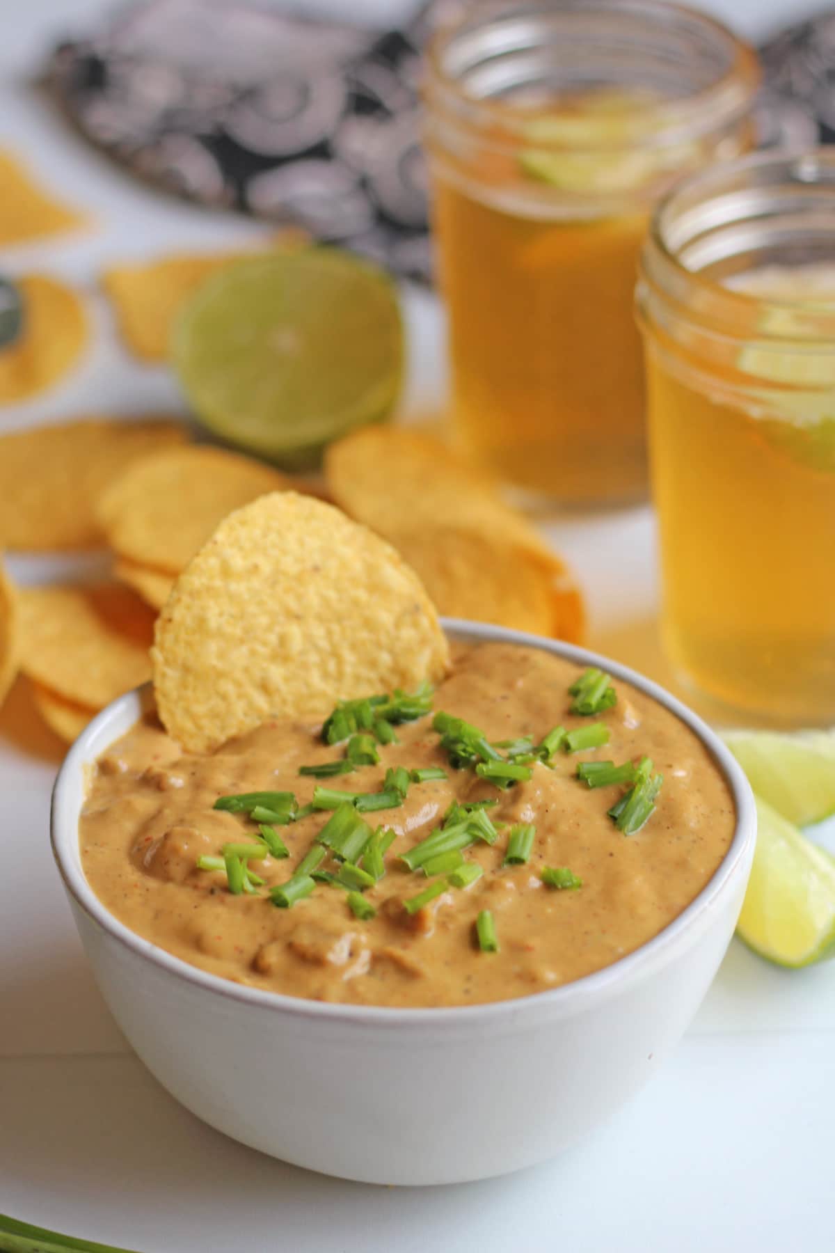Vegan chili cheese dip in white bowl by beer and tortilla chips.