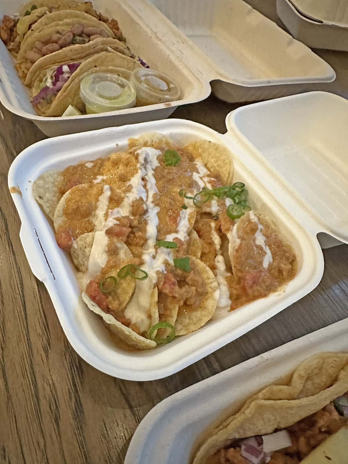 Nachos with crema drizzle in cardboard container.