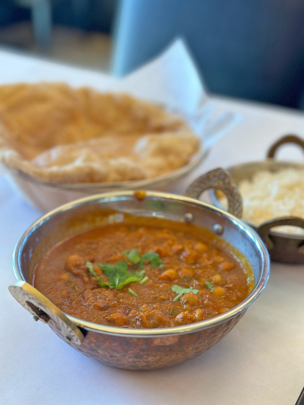 Punjabi chole in metal bowl by rice and bread.