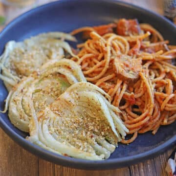 Slices of roasted fennel by pasta with red sauce in blue bowl.