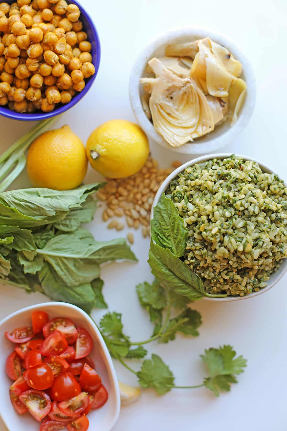 Bowl of pesto rice by roasted chickpeas, lemons, basil, cilantro, pine nuts, artichoke hearts, cherry tomatoes, and garlic.