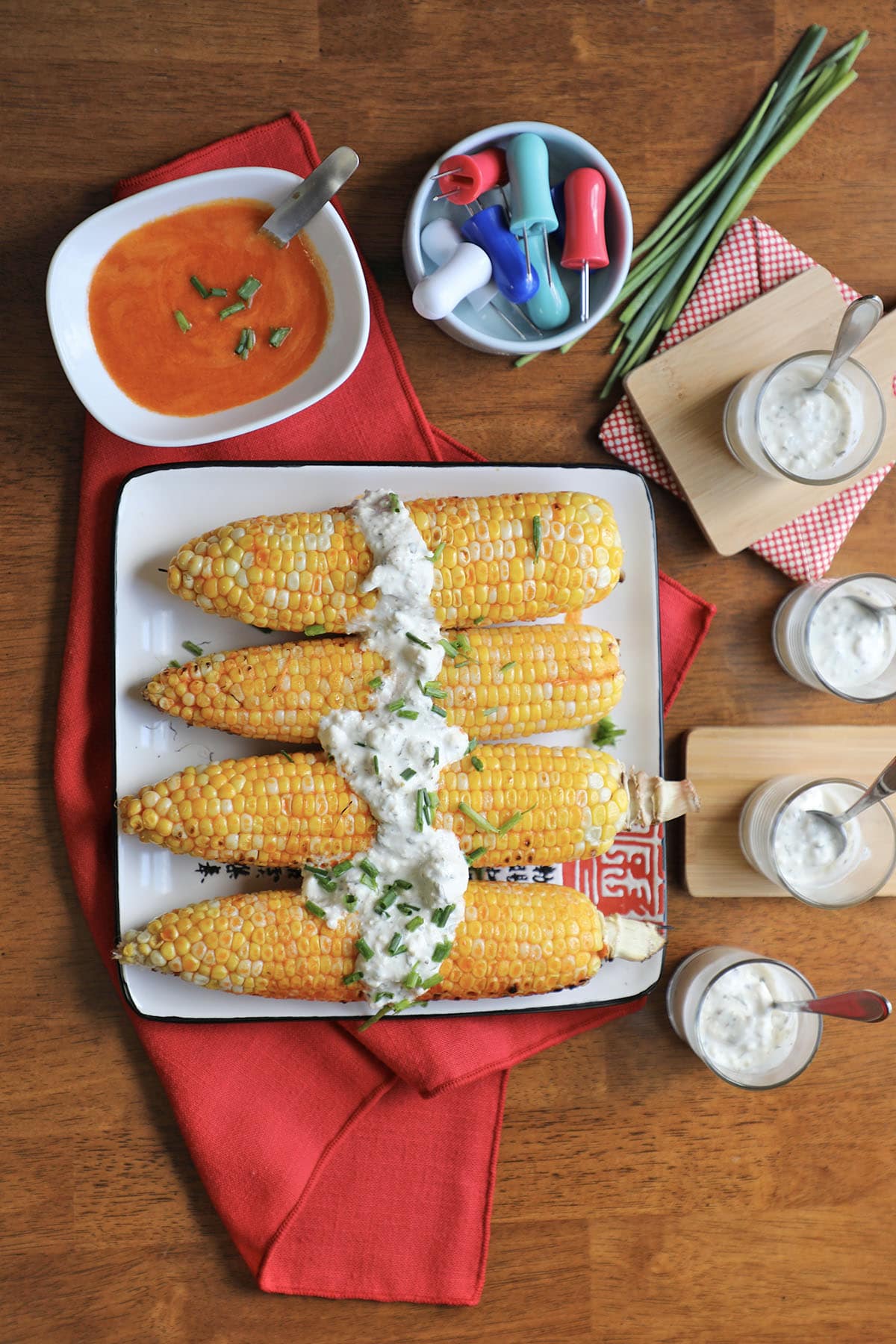 Platter with ears of corn topped with vegan blue cheese dressing by corn holders, buffalo sauce, and dip cups.
