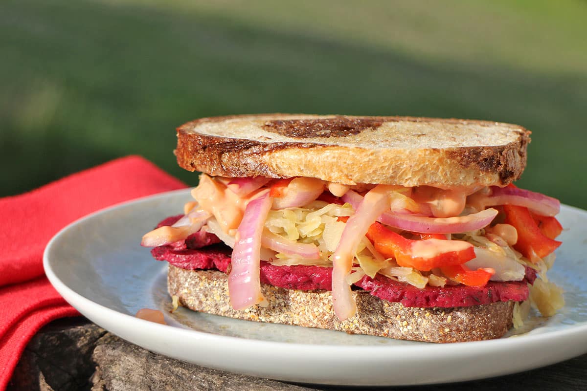Close-up seitan reuben sandwich with onions, peppers, and sauerkraut.