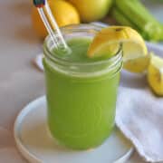 Glass filled with cucumber celery apple juice with a lemon wedge on rim.