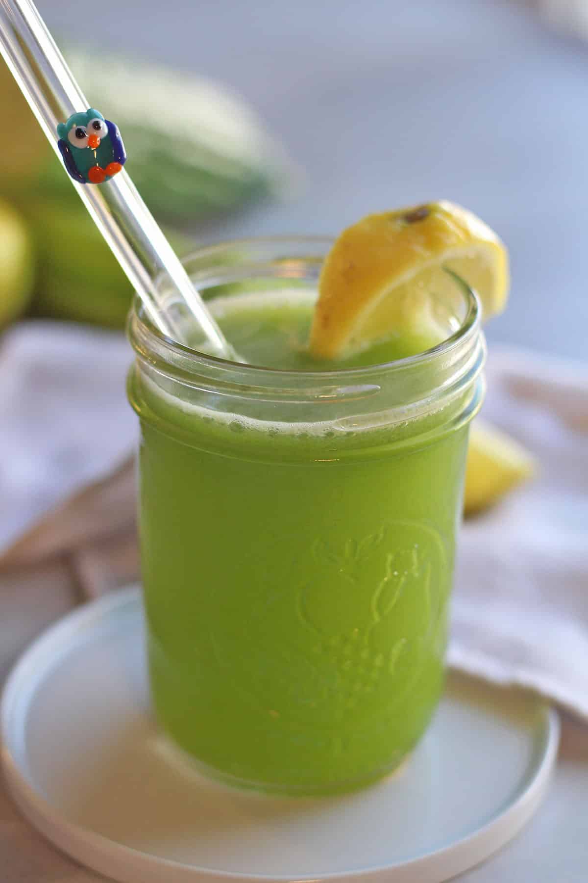 Glass straw in celery cucumber juice with lemon slice on rim.