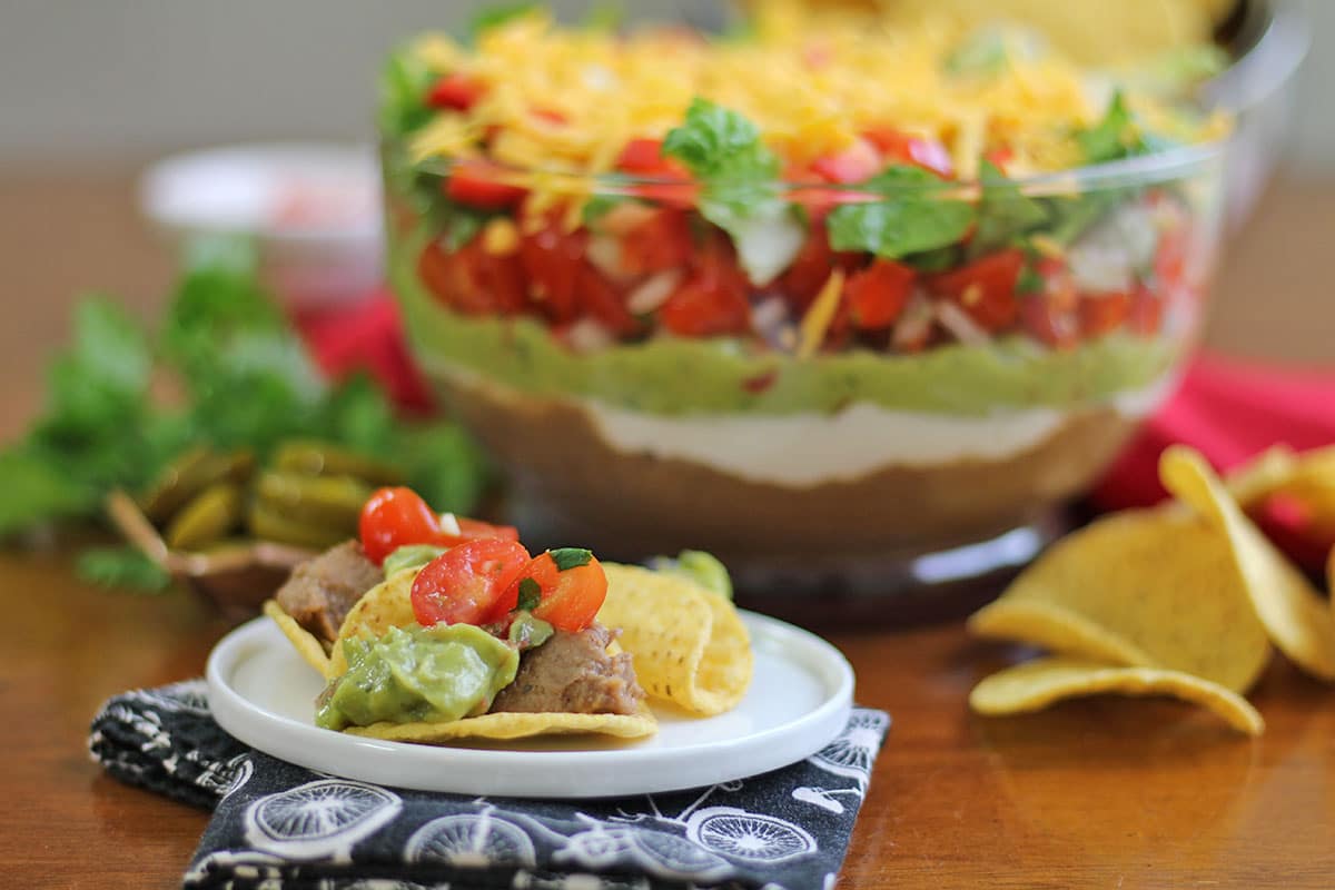 Tortilla chips topped with refried beans, salsa, and guacamole by bowl of dip.