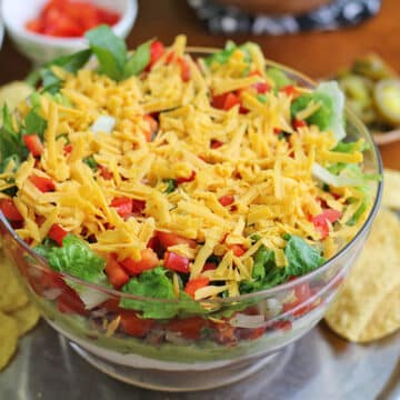 Glass bowl with vegan 7 layer dip surrounded by tortilla chips.
