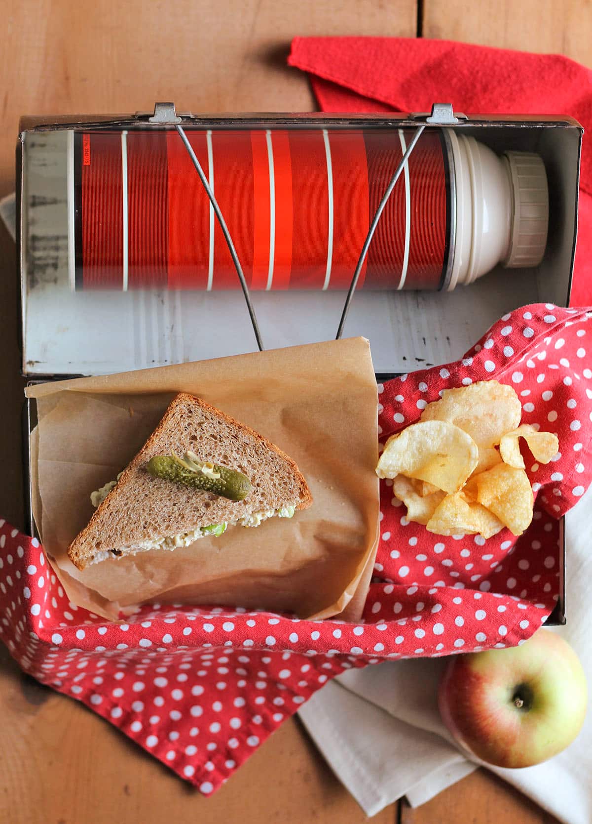 Lunchbox with thermos, apple, potato chips, and vegan egg salad sandwich.