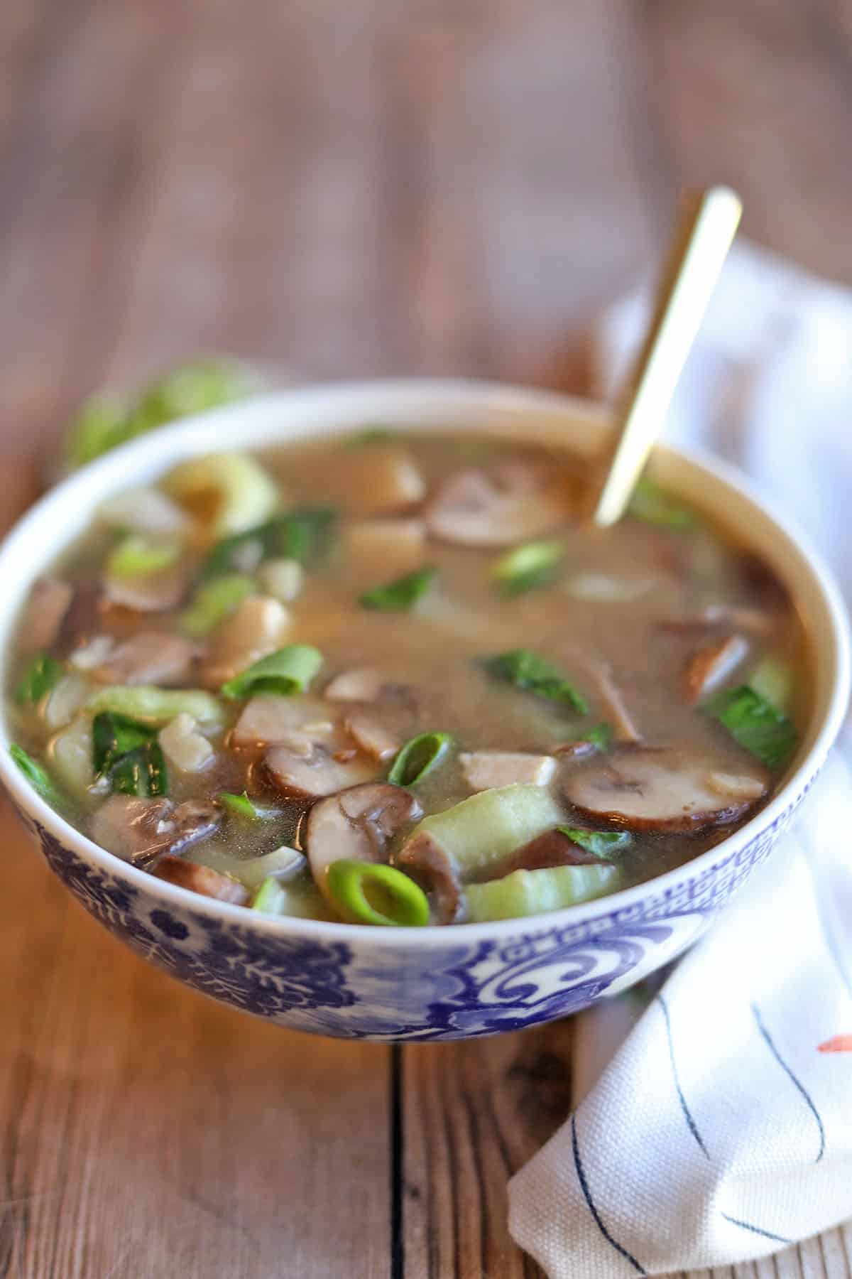 Miso soup with mushrooms in bowl with gold spoon.