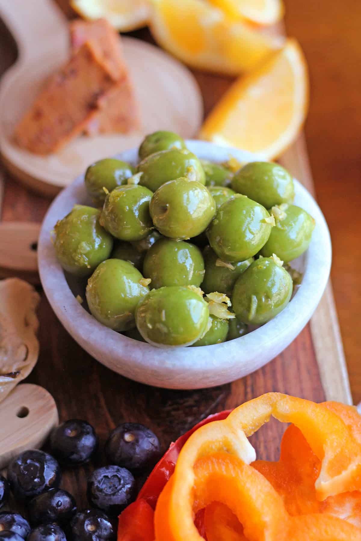 Shiny Castelvetrano olives in bowl by berries and bell peppers.