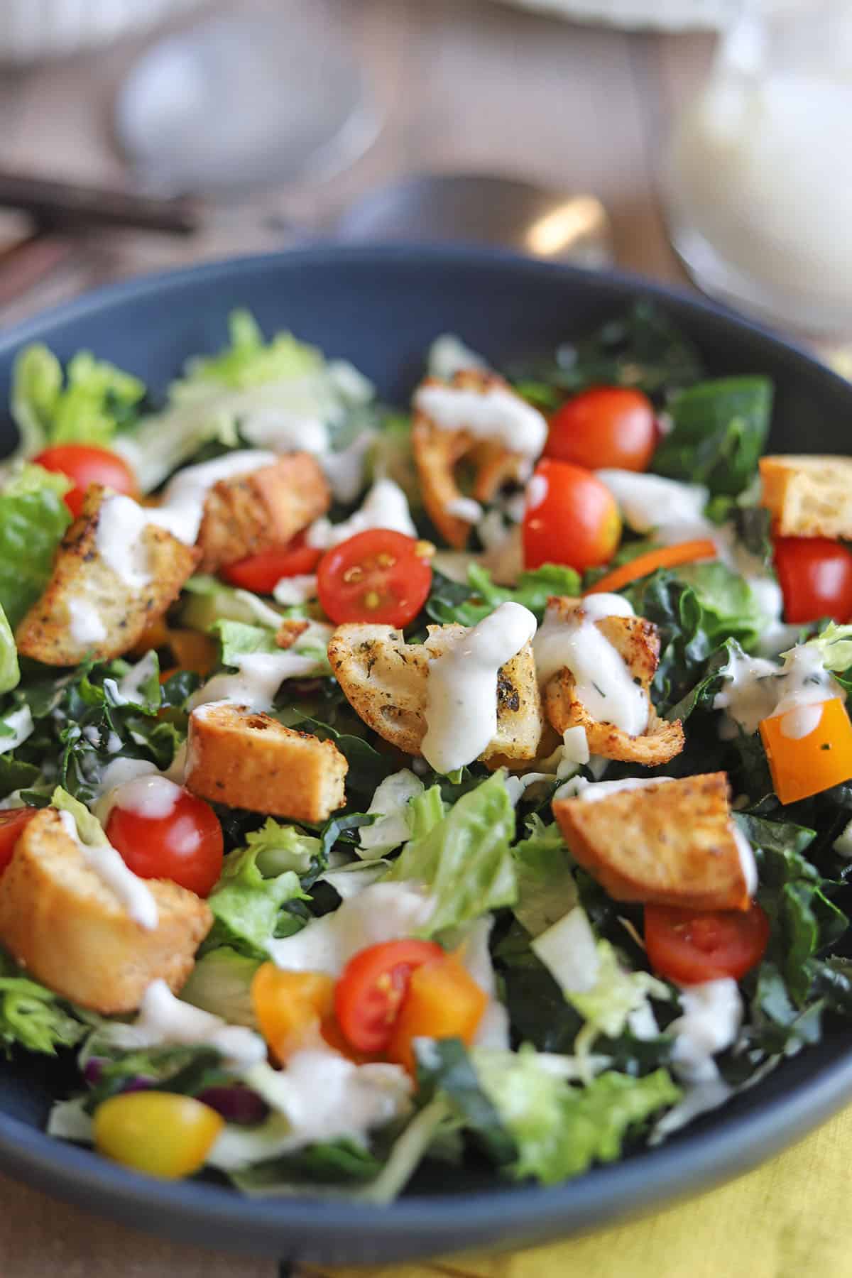 Close-up ranch dressing drizzled over homemade croutons in salad.