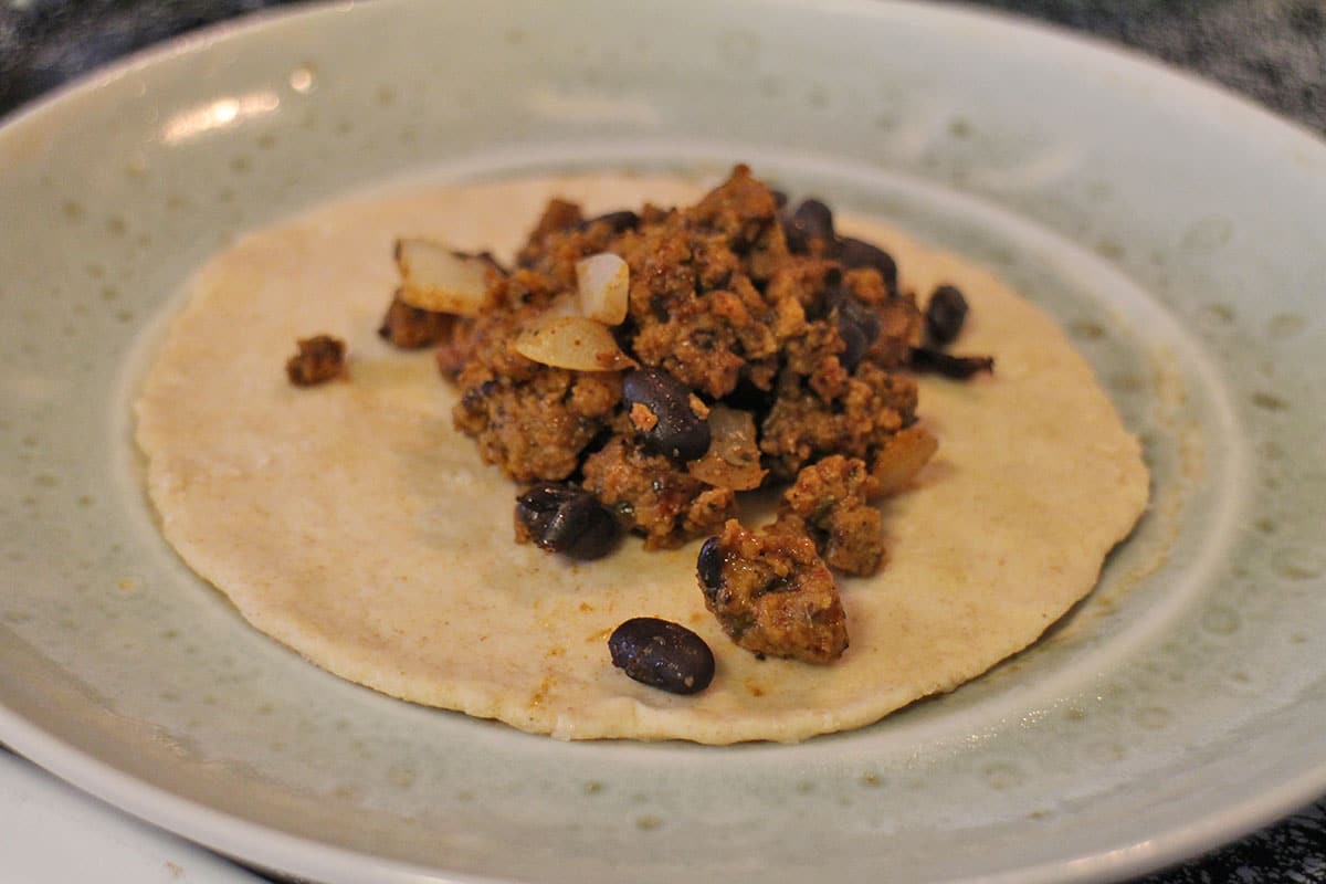Vegan chorizo and bean mixture on open taco shell dough.