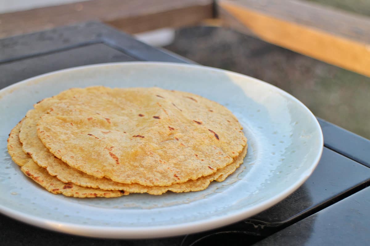 Grilled corn tortillas on plate outside.