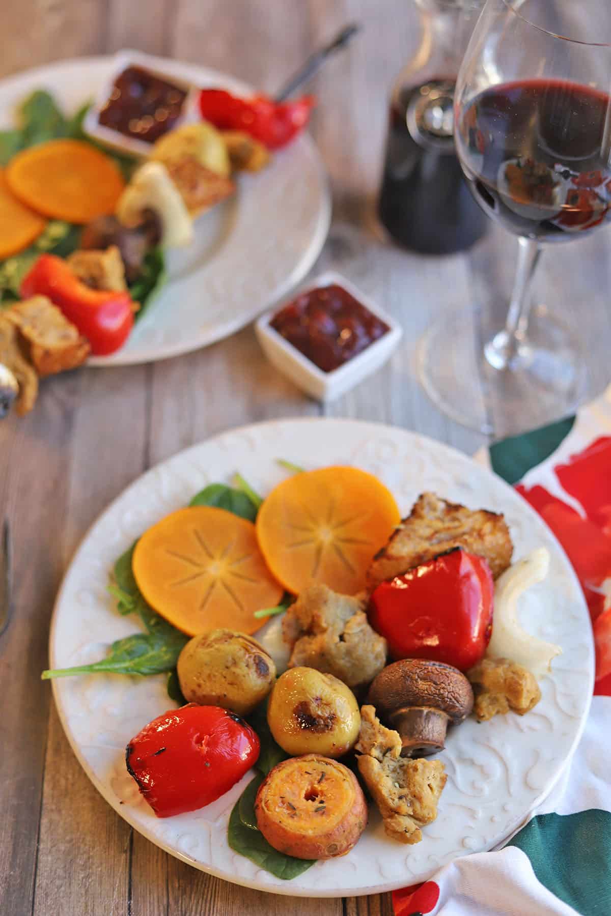 Grilled vegetables and seitan on plate by glass of wine.