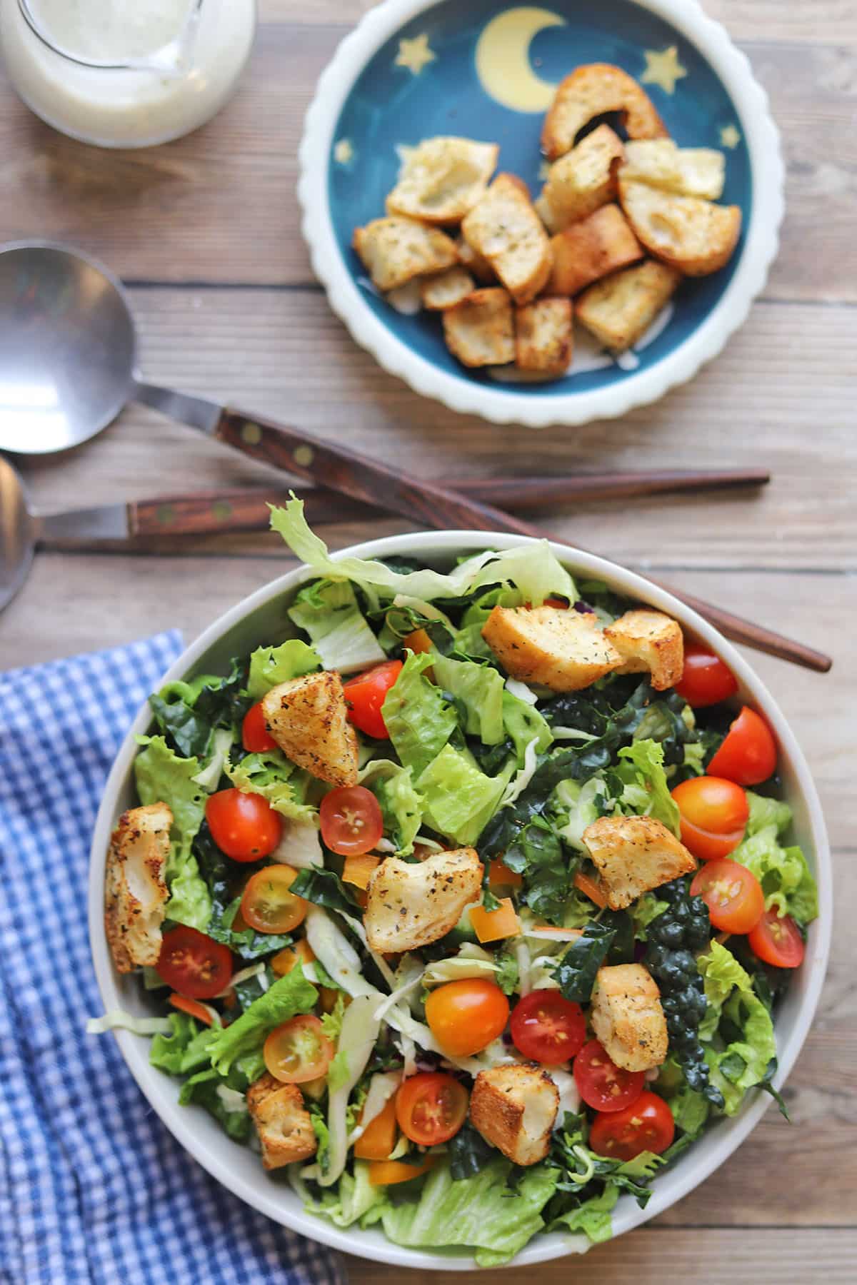 Salad with croutons in large bowl by serving utensils.