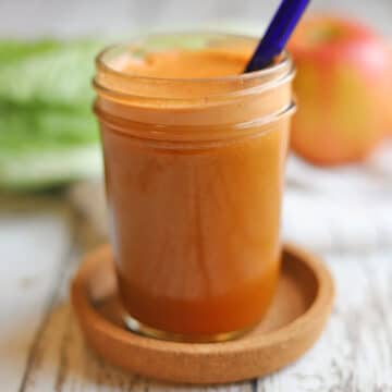 Bright orange colored carrot apple juice in glass with blue straw.