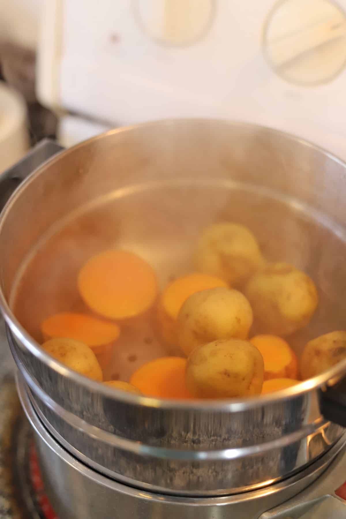 Potatoes and sweet potatoes steaming in metal pot.